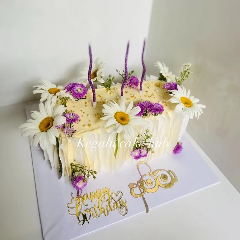 Rectangular cream slab cake with daisy and lilac flowers and gold happy birthday toppers