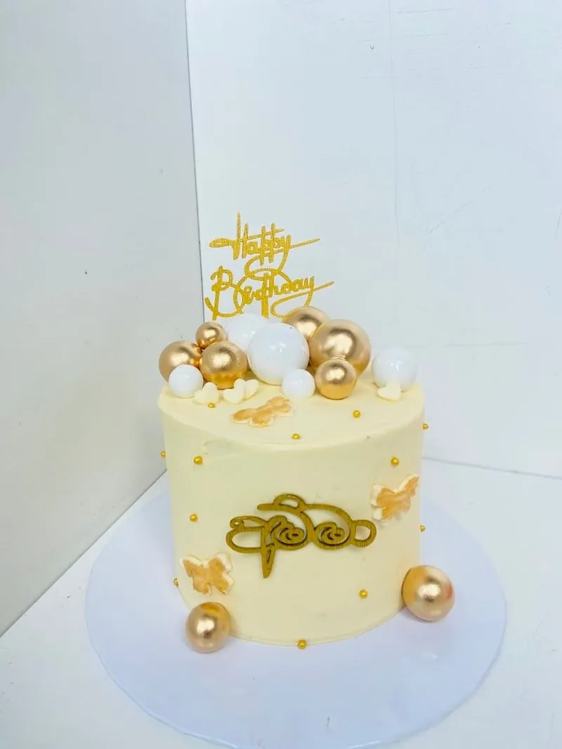 Cream celebration cake with gold and pearl balloon decorations and a gold happy birthday topper