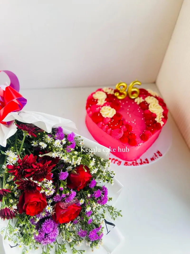 Heart-shaped pink birthday cake with piped cream roses, gold number topper and a bouquet of flowers