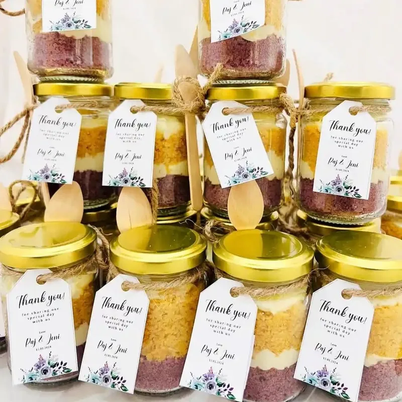 Glass jars filled with layered cake and buttercream, tied with twine and thank-you tags