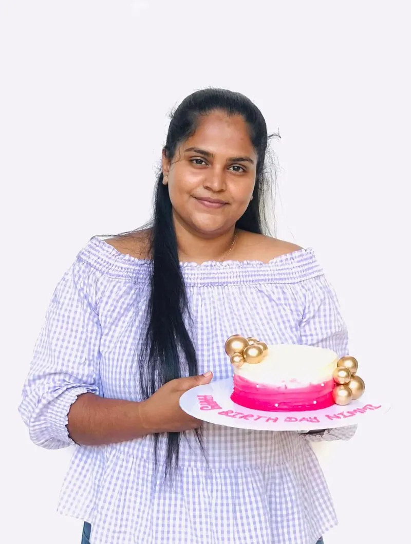 Cake maker holding a pink and cream celebration cake with gold decorations