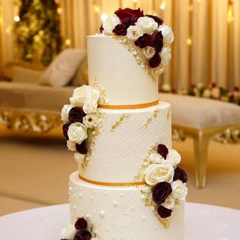Three-tier ivory wedding cake with textured detailing, burgundy roses and gold accents